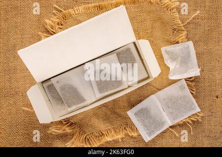 Mehrere aromatische Teebeutel in einer Papierkiste auf einem Jutetuch, Makro, Draufsicht. Stockfoto