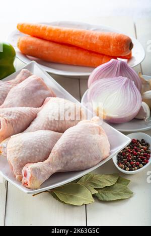 Rohe Hähnchenbeine mit Gemüse zum Kochen auf dem Küchentisch Stockfoto