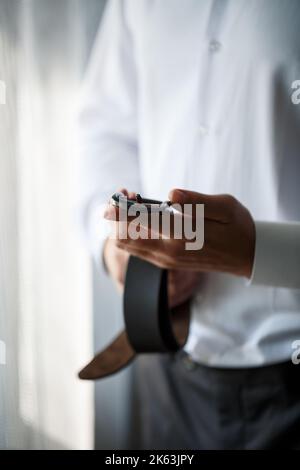 Eleganter Geschäftsmann Mann, der einen Gürtel an seiner Hose befestigt er Trägt ein weißes Hemd Stockfoto