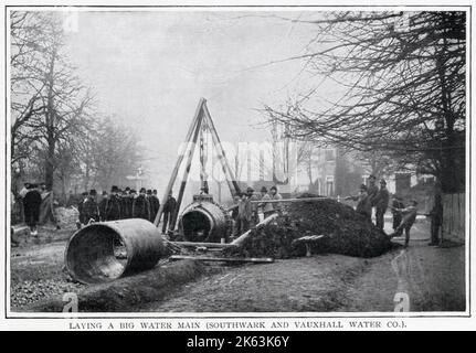 Das Foto zeigt Ingenieure und Assistenten, die schwere, kreisförmige Rohrleitungen mit einem Kran in den Straßen von Süd-London unterirdisch anheben. Das war eine gewaltige Aufgabe, die in ganz London stattfand, um die Gemeinde mit frischem Wasser zu versorgen. Stockfoto