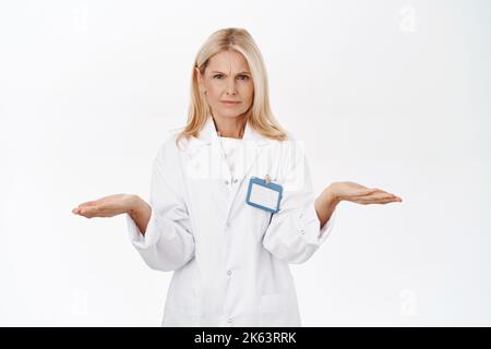 Doktor sieht verwirrt aus, zuckende Schultern mit besorgtem Gesicht, stehend über weißem Studiohintergrund Stockfoto