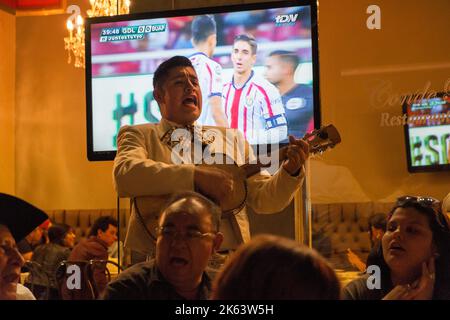 Mariachi-Sänger sang in einer Bar in Guanajuato, Mexiko, Fußballspiel im Fernsehen hinter ihm Stockfoto