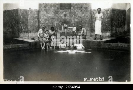 Sieben Männer und zwei Jungen sitzen in und um eines der natürlichen Thermalbäder in Bursa, Türkei. Die heißen Quellen und Thermalbäder im Bezirk Cekirge sind reich an verschiedenen natürlichen Heilmitteln wie Schwefel und Eisen und reich an Magnesium. Diese Quellen sind aufgrund ihrer kristallklaren Sicht auch als „silver Waters“ bekannt. Stockfoto