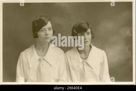 Studio-Porträt von zwei Frauen, beide mit dunklem Haar und identischen Blusen mit großem Kragen und Krawatte. Stockfoto