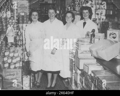 Vier Ladenarbeiter stellen sich für ein Foto in einem gut bestückten Lebensmittelgeschäft auf. Das Rationierungszeichen dahinter und die königliche Dose deuten darauf hin, dass das Foto auf etwa 1952 oder 1953 datiert ist (die Rationierung endete 1954 in Großbritannien). Stockfoto