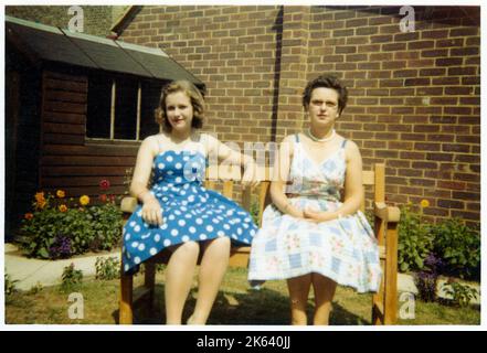 Eine Mutter und ein Duaghter in ihren besten Sommerkittel, die auf einer Bank in einem sehr gepflegten und gepflegten Vorstadtgarten sitzen - August 1959. Stockfoto