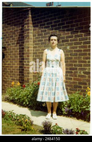 Eine Frau mittleren Alters stehend (sehr!) Stifly auf einem Pfad entlang einer wunderschön gepflegten Vorstadt Garten Blumenbeet - August, 1959 Stockfoto