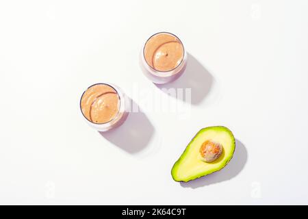 Zwei Gläser mit Avocado-Schokolade-Smoothie mit Zutaten auf weißem Hintergrund. Draufsicht, flach liegend Stockfoto