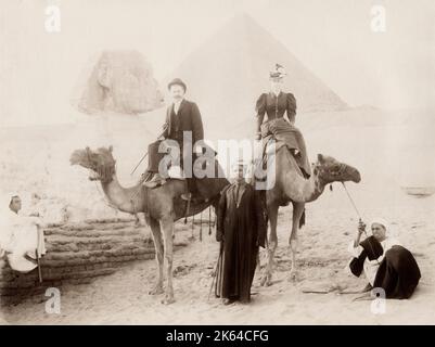 Vintage 19. Jahrhundert Foto - Touristen auf Kamelen mit Führern, Besuch der Sphinx und große Pyramide von Gizeh, Gizeh, Kairo, Ägypten, Bild c. 1890/1900. Stockfoto