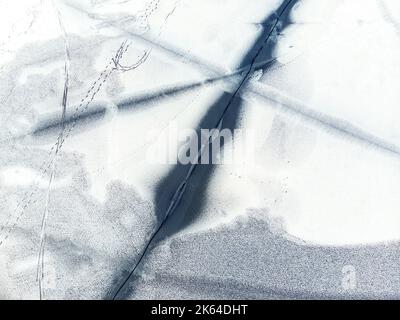 Luftdrohne Draufsicht auf schneebedeckten gefrorenen See oder Fluss Oberfläche mit großen rissigen Eis diagonalen Linien. Natürliche Winterlandschaft abstrakte Textur Stockfoto