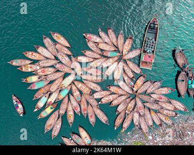 Dhaka, Dhaka, Bangladesch. 11. Oktober 2022. Eine Flotte von Holzbooten, die den Blütenblättern ähneln, wartet darauf, Pendler über den Buriganga River zu Jobs an einem großen Flusshafen in Dhaka, Bangladesch, zu bringen, während Bootsmänner die Boote in einem blumigen Muster zusammenbinden und vor der Nachmittagsverkehrszeit vierzig Augenzwinkern bekommen. Sie arbeiten 16 Stunden am Tag und erhalten weniger als Â£5 dafür. So ruhen sie sich aus, wenn sie die Chance haben, die Müdigkeit der langen Arbeitszeiten zu lindern. Während dieser Zeit werden die meisten Boote mit Ausnahme einiger weniger zusammengebunden und die Anzahl der Passagiere ist niedriger als t Stockfoto