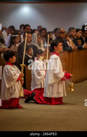 Auf den Knien nehmen multirassische Altarjungen an einer katholischen Messe in Tustin, CA, Teil. Stockfoto