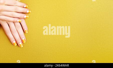 Schöne weibliche Hände mit orangefarbener Maniküre wie Candy Corn. Gepflegte Nägel mit gelbem Gelpolitur. Halloween-Style Stockfoto