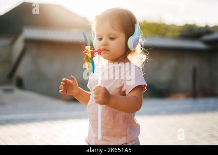 Das Mädchen, das draußen mit einem Wettervane in der Hand steht und glücklich auf ihr neues Spielzeug schaut. Glückliche Kindheit und Baby Gesundheit. Porträt von niedlich Stockfoto