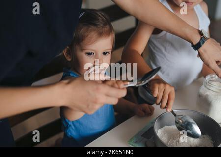 Liebevolle Mutter lehren kleine Tochter backen in der Küche, bereiten Pfannkuchen oder Kekse, zu Hause zusammen. Glückliche Familie in der Küche. Wochenende. Gebäck Stockfoto