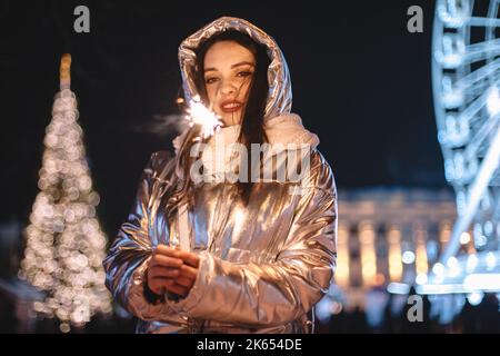 Junge Frau, die während der Weihnachtsferien in der Nacht auf dem Stadtplatz steht und einen Funker hält Stockfoto