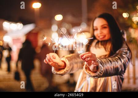 Junge Frau, die zu Weihnachten in der Stadt steht und Wunderkerzen in der Hand hält Stockfoto