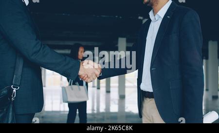 Nahaufnahme von Männern, die sich nach einem erfolgreichen Immobilienvertrag in einem geräumigen Industriegebäude die Hände schüttelten. Geschäfts- und Vertragskonzept. Stockfoto