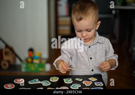 Porträt eines niedlichen kleinen Jungen, der mit Buchstaben und Zahlen auf einem Tisch spielt Stockfoto