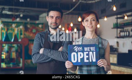 Glücklich attraktive Leute Café-Arbeiter in Schürzen halten ja, wir sind offen Schild und lächeln, während im Coffee Shop stehen. Eröffnung neuer Geschäfte und Start-up-Konzept. Stockfoto