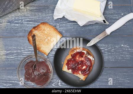 Traditionelles Landfrühstück, Toast mit Marmelade und Butter auf rustikalem Holztisch. Draufsicht. Stockfoto