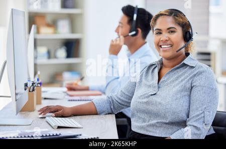 Junge, glückliche, gemischte Rasse, weibliche Callcenter-Agentin, die an einem Computer arbeitet, während sie Anrufe in einem Büro bei der Arbeit entgegennimmt. Hispanische weibliche Kundenbetreuung Stockfoto