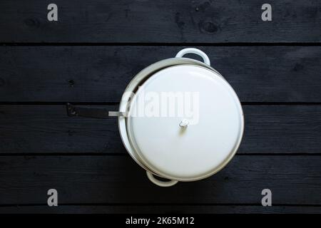Weißer selbstgemachter Auflauf mit Suppe mit Deckel steht auf schwarzem Holztisch, Auflauf mit Deckel Stockfoto