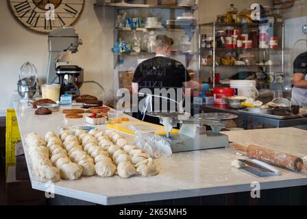 Blick durch das Fenster einer Frau, die in einer handwerklichen Bäckerei arbeitet. Blick durch ein Backwarenfenster von außen. Storefront. Editorial, Straßenfoto Stockfoto