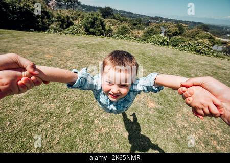 Nahaufnahme des kleinen Jungen, der von den Eltern draußen in der Natur herumgeschwenkt wird. POV Aufnahme eines kleinen Jungen, der vorgibt zu fliegen und Spaß während des Vaters zu haben Stockfoto