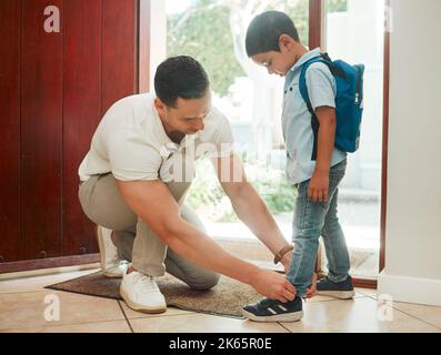 Vater und Sohn passen die Schuhe zu Hause an und bereiten sich auf den ersten Schultag vor. Papa kleidete seinen niedlichen kleinen Jungen an der Tür, bevor er das Haus verließ Stockfoto