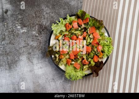 Gurkensalat mit Lachs, Salat und ihrem Salat auf einem runden Teller auf dunkelgrauem Hintergrund. Draufsicht, flach liegend Stockfoto