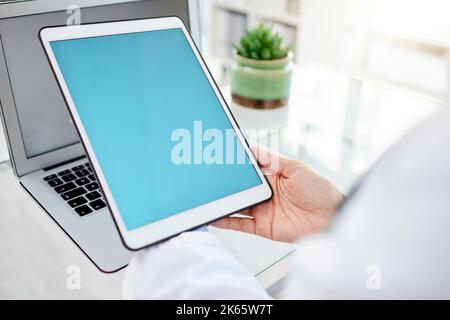 Unbekannte Frau mit gemischter Rasse, die ein Tablet benutzte und eine E-Mail tippte, während sie an ihrem Schreibtisch in einem Krankenhaus saß. Ärztin, die ein drahtloses Gerät verwendet, während Stockfoto