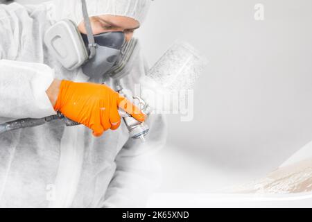 Sprühmaler im Schutzhandschuh mit Airbrush-Pulverisierer zur Lackierung der Karosserie in der weißen Lackkammer. Stockfoto