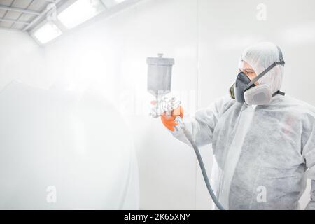 Männlicher Arbeiter, der ein Auto in einer weißen Lackierkabine malt. Stockfoto