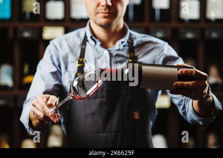Sommeliermännchen gießt Rotwein in langstielige Weingläser. Stockfoto