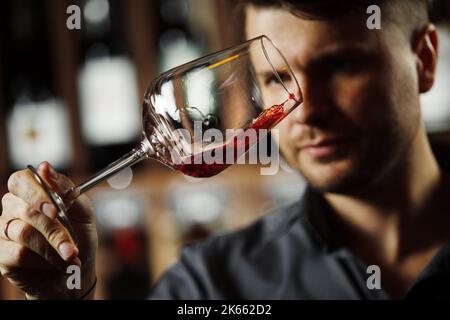 Bokal von Rotwein auf dem Hintergrund, männliche Sommelier schätzen Getränk Stockfoto