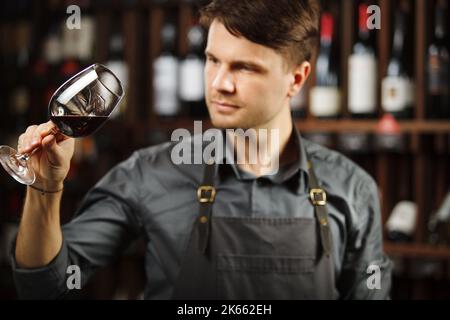 Bokal von Rotwein auf dem Hintergrund, männliche Sommelier schätzen Getränk Stockfoto