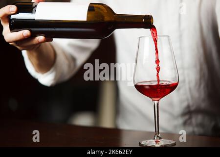 Sommeliermännchen gießt Rotwein in langstielige Weingläser. Stockfoto