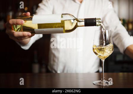 Sommeliermännchen gießt Weißwein in langstielige Weingläser. Stockfoto