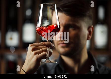 Bokal von Rotwein auf dem Hintergrund, männliche Sommelier schätzen Getränk Stockfoto