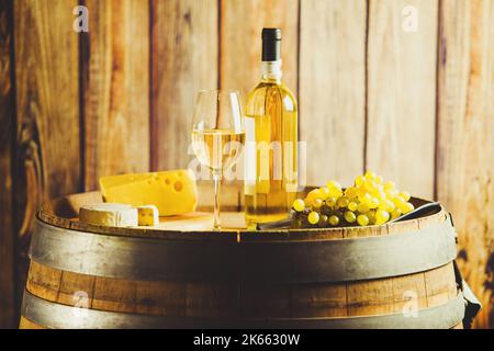Weißwein auf Fass mit Traube und Käse auf dem Hintergrund einer Holzwand. Stockfoto