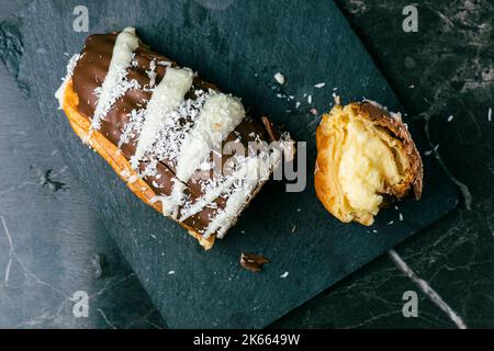 Hausgemachtes Eclair mit Mango- und Kokosnuss-Schlagsahne. In Milchschokolade getaucht. Stockfoto