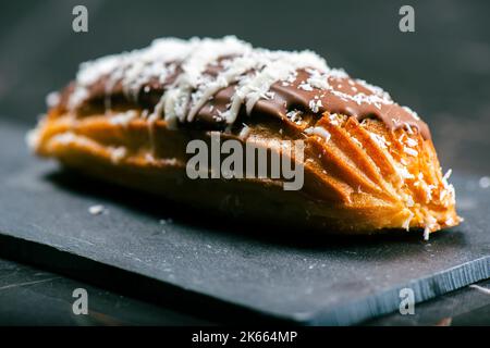 Hausgemachtes Eclair mit Mango- und Kokosnuss-Schlagsahne. In Milchschokolade getaucht. Stockfoto