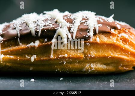 Hausgemachtes Eclair mit Mango- und Kokosnuss-Schlagsahne. In Milchschokolade getaucht. Stockfoto