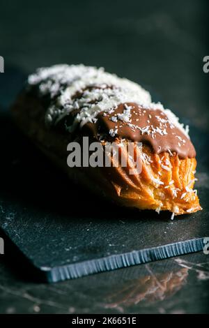 Hausgemachtes Eclair mit Mango- und Kokosnuss-Schlagsahne. In Milchschokolade getaucht. Stockfoto