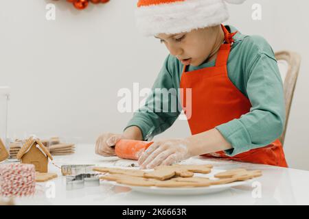 Ein süßer Junge in einem Weihnachtsmütze macht Neujahrskekse in der Küche. Heiligabend, Silvester. Stockfoto