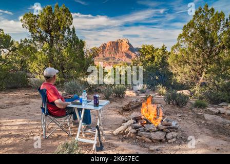 Mann am Lagerfeuer bei Sonnenuntergang, im Pinyon Wacholderwald vor der Smithsonian Butte Road, Canaan Mtn Wilderness, Mount Kinesava im Zion National Park in dist, Utah Stockfoto