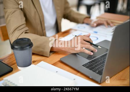 Intelligenter asiatischer Geschäftsmann oder männlicher Chef, der an seinem Schreibtisch arbeitet, mit einem Laptop sein Projekt auf einem Notebook-Computer macht Stockfoto