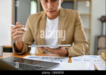 Professionelle Millennial asiatischen Geschäftsmann oder Finanzberater mit digitalen Tablet und die Arbeit an seinen finanziellen Papierkram im Büro. Cropped i Stockfoto