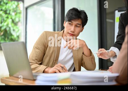Ein kluger und gutaussehender, tausendjähriger asiatischer Geschäftsmann oder männlicher Finanzanalyst konzentrierte sich beim Treffen auf die Betrachtung der Finanzdaten auf dem Laptop-Bildschirm Stockfoto